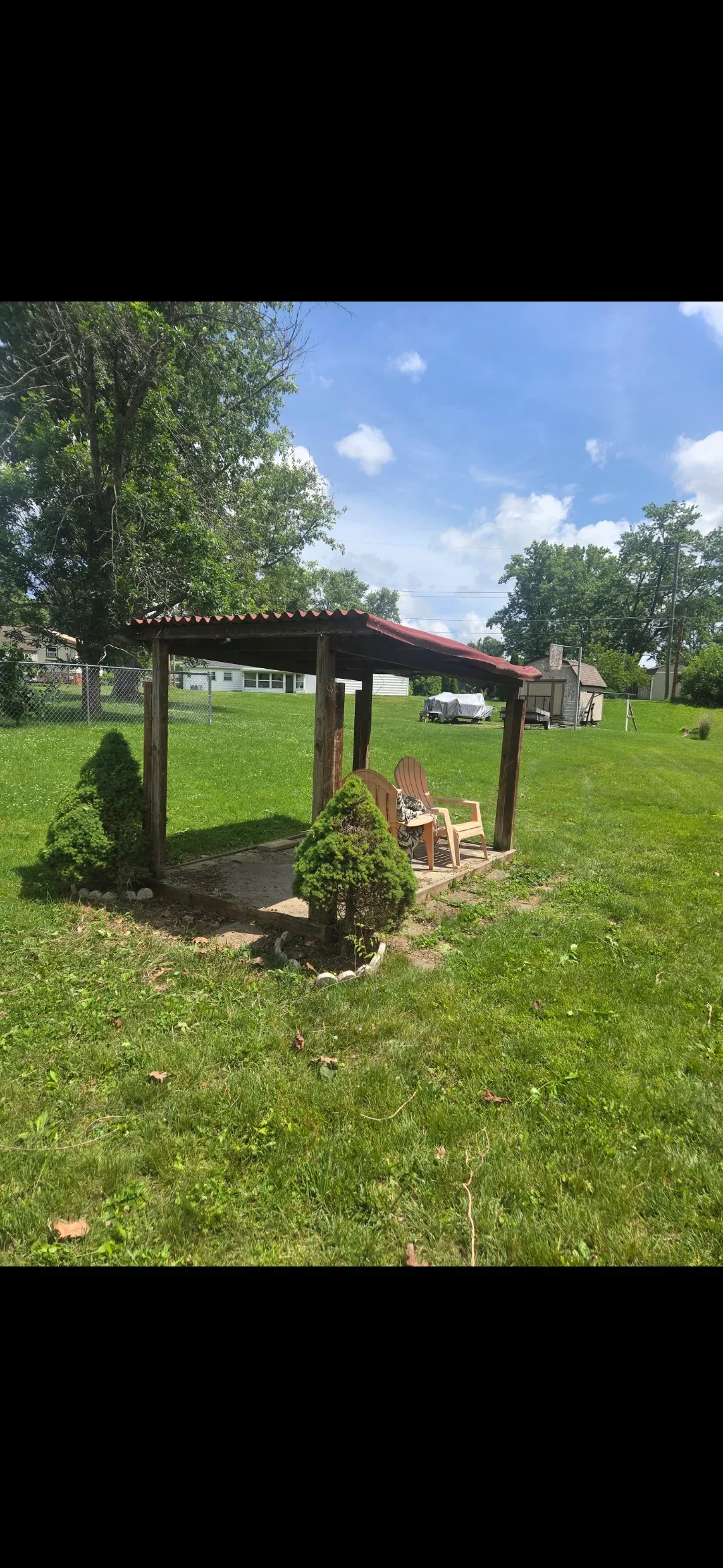Wooden pergola with red roof, landscaped lawn, shrubs, and Adirondack chairs