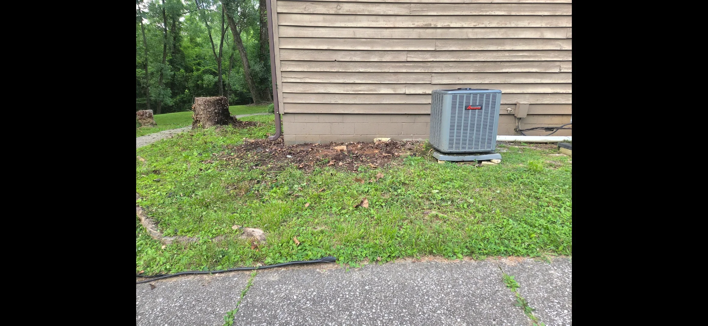 New HVAC condenser unit installed on prepared ground next to house with mulch bed and healthy lawn